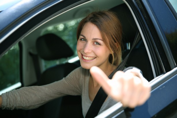 Cheerful girl sitting inside car with thumb up